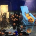 A goldfish suffering from swim bladder disease rests on a wooden chair in a fish tank.