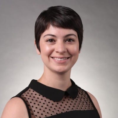 A woman with short hair and a collared top smiling against a gray background, specializing in aquatic veterinary services.